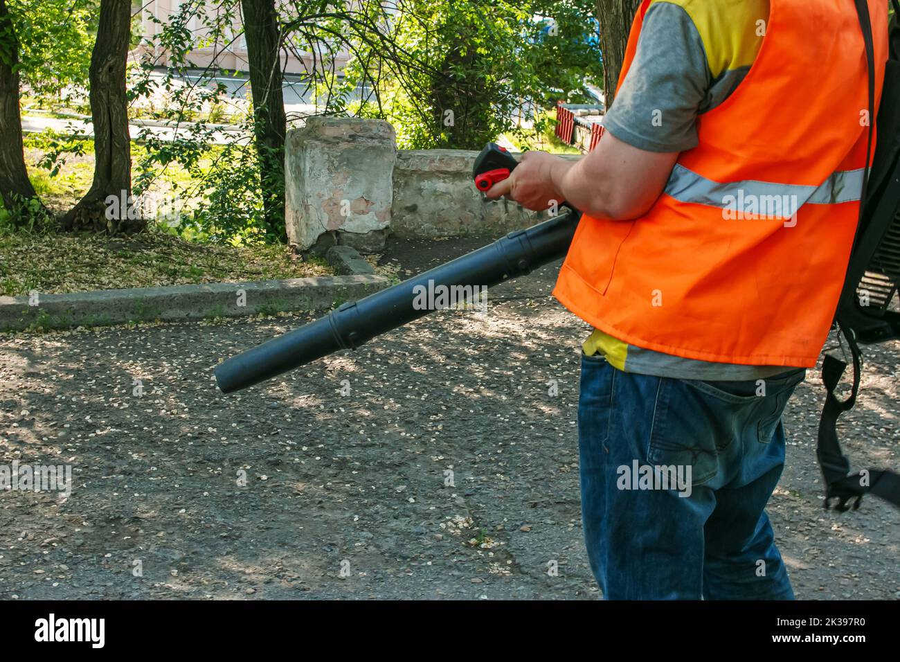 Reinigung von fallenden Blättern im Stadtpark während der sonnigen Trockenzeit im Frühjahr. Verwendung eines Gebläses zur Reinigung im Park. Das Konzept der Saisonarbeit. Stockfoto