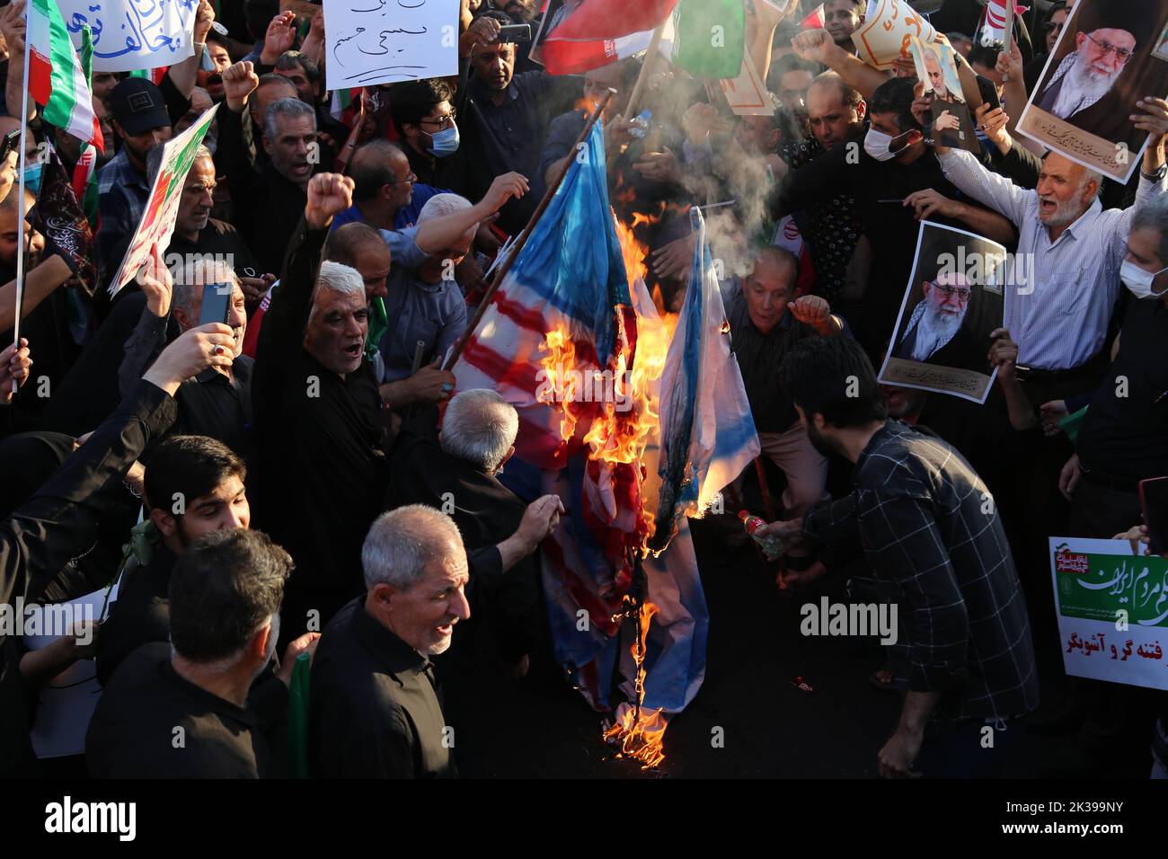 Teheran, Teheran, Iran. 25. September 2022. Regierungsnahe Demonstranten verbrennen während einer Kundgebung Darstellungen der britischen, israelischen und US-amerikanischen Flaggen, um die jüngsten regierungsfeindlichen Unruhen wegen des Todes einer jungen Frau in Polizeigewahrsam in Teheran, Iran, am 25. September 2022 zu verurteilen. Die Krise, die sich im Iran ausbreitet, begann als öffentliche Ausschüttung über den Tod von Mahsa Amini, einer jungen 22-jährigen Frau aus Saqqez, einer nordwestlichen kurdischen Stadt, die letzte Woche von der Moralpolizei des Landes in Teheran verhaftet wurde, weil sie angeblich gegen die strikt erzwungene Kleiderordnung verstoßen hatte. Kredit: ZUMA Press, Inc./Alamy Live Nachrichten Stockfoto