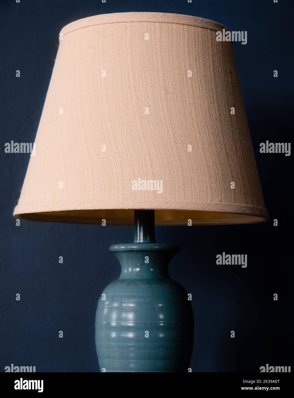 Hellblaue Lampe mit braunem Lampenschirm vor einem arkblauen Hintergrund Stockfoto