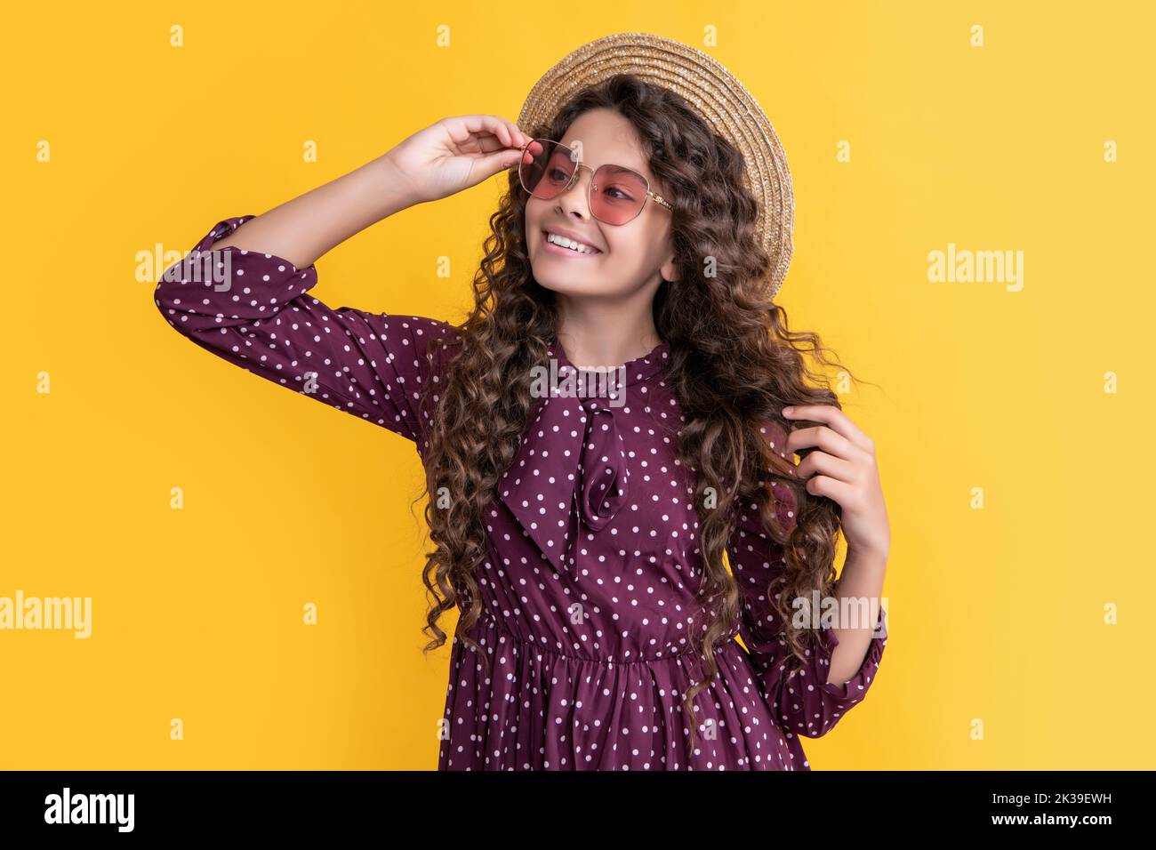Glückliches Mädchen in Strohhut und Sonnenbrille mit langen Brünette lockiges Haar auf gelbem Hintergrund Stockfoto
