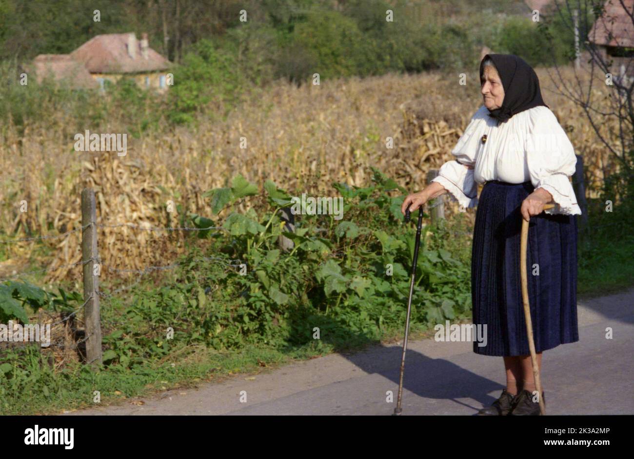Poșaga, Kreis Alba, Rumänien, ca. 1999. Ältere Frau in traditioneller schwarz-weißer Kleidung, die mit Hilfe von zwei Stöcken zu Fuß geht. Stockfoto