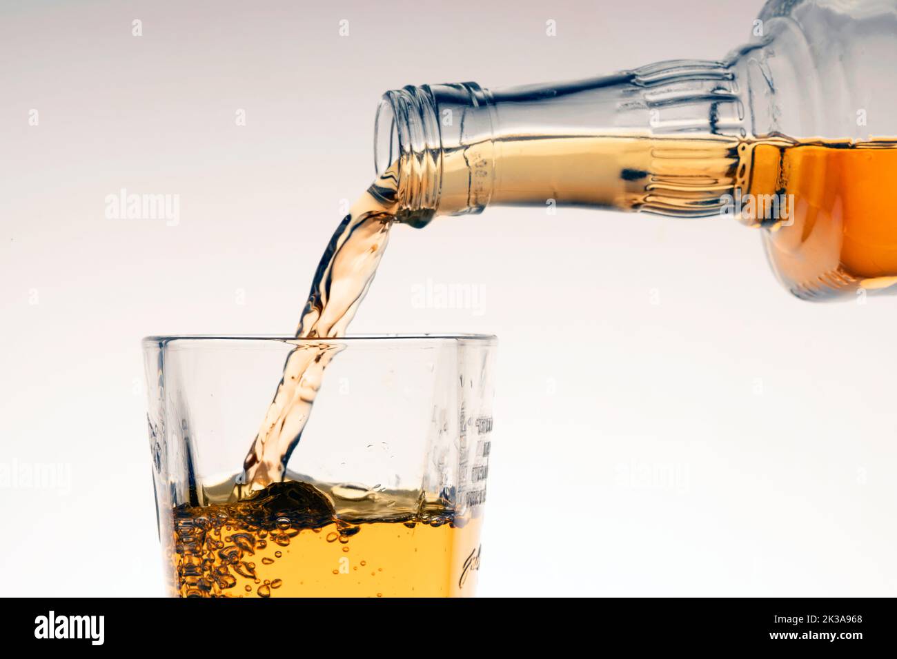 Gießen Sie Whiskey oder Bourbon in ein Glas auf beige weißem Hintergrund. Stockfoto