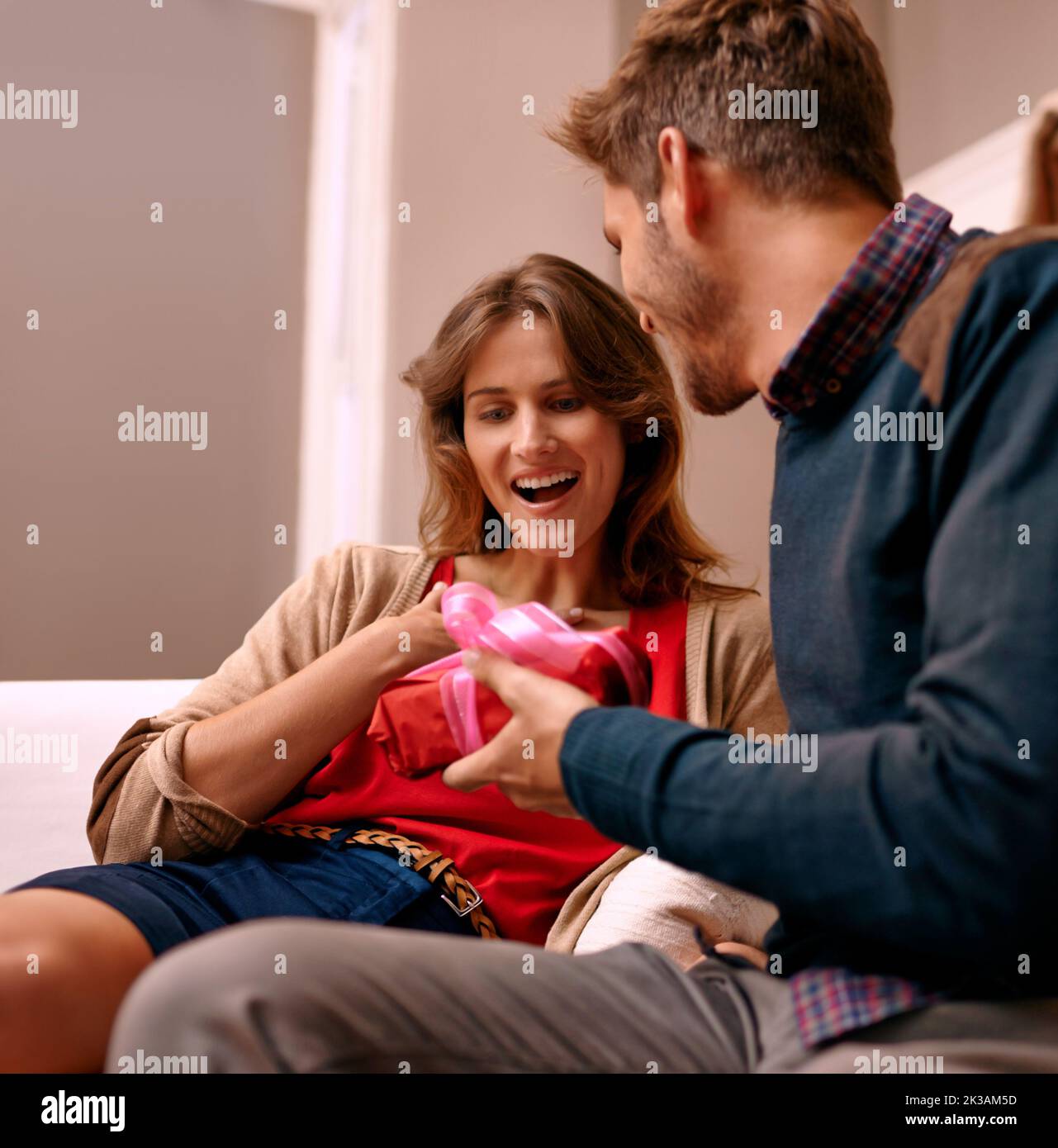 Das Schenken ist das größte Geschenk von allen... Eine junge Frau erhält ein weihnachtsgeschenk von ihrem Mann. Stockfoto