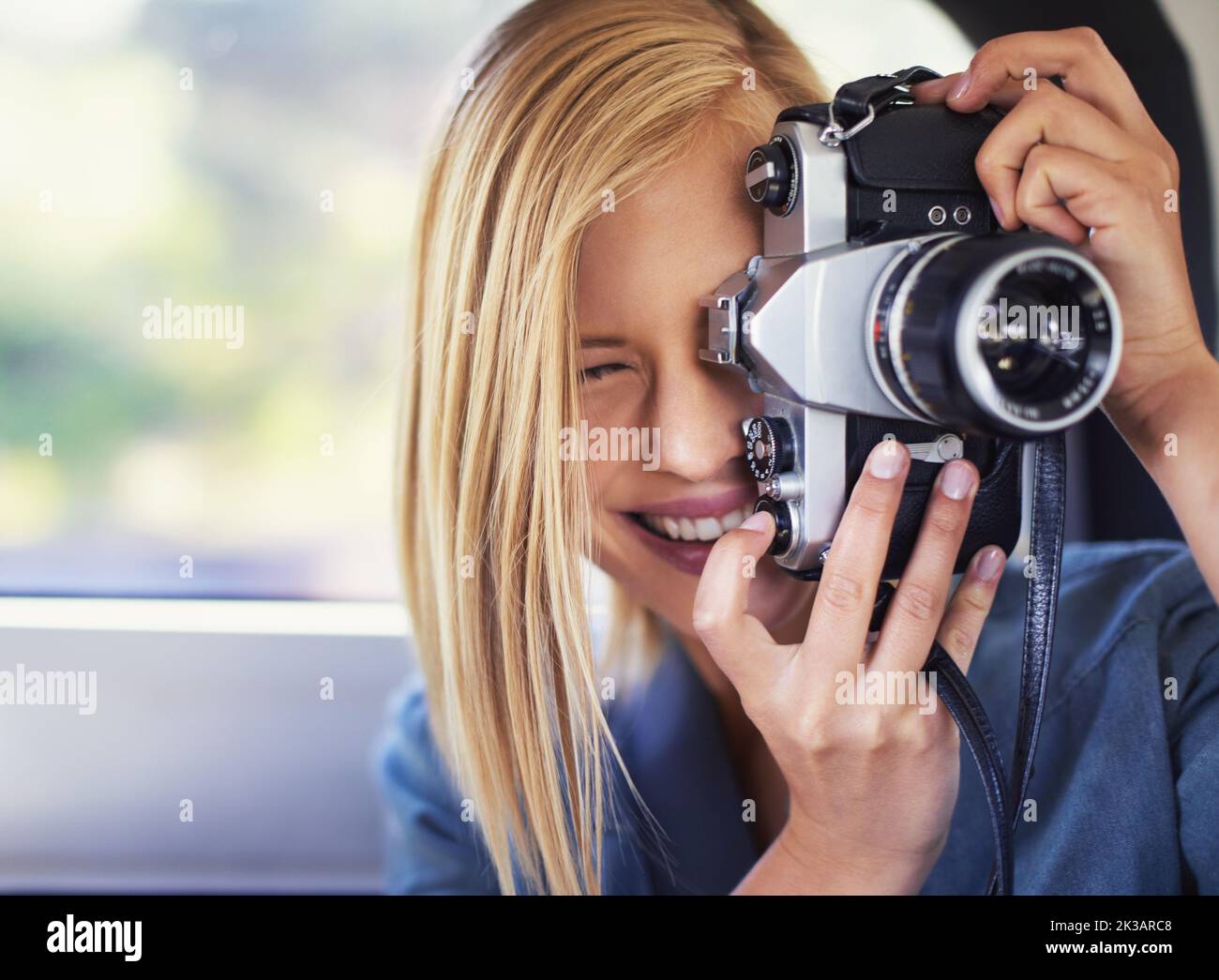 Die perfekte Momentaufnahme. Eine attraktive junge Frau, die in einem Auto sitzt und mit einer alten Kamera fotografiert. Stockfoto