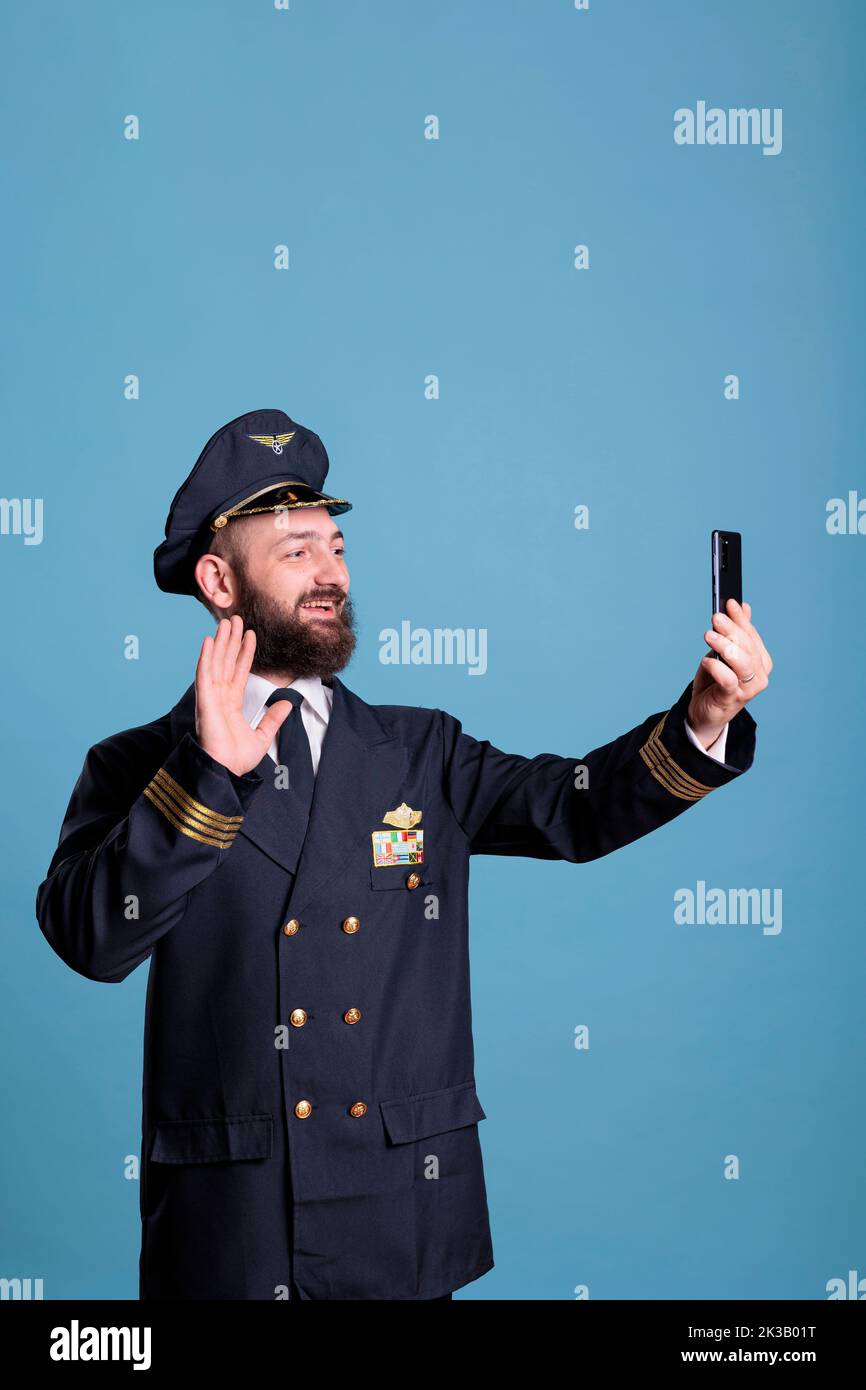 Ein Flugzeugflieger begrüßt Remote-Mitarbeiter des Flugpersonals während eines Online-Videocall-Meetings mit einem modernen Smartphone. Pilot trägt Fluguniform, plaudert vor dem Flug, mittellange Aufnahme Stockfoto