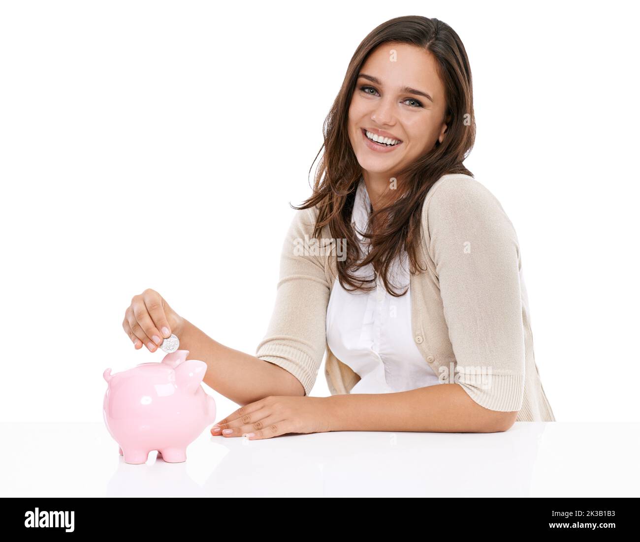 Keine Einsparungen zu gering. Studioporträt einer jungen Frau, die Münzen in ein Sparschwein eingibt. Stockfoto