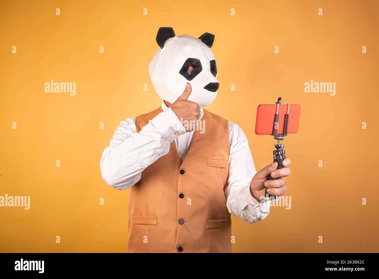 Mann in Pandabärmaske mit Smartphone bei einem Videoanruf auf gelbem Hintergrund. Stockfoto