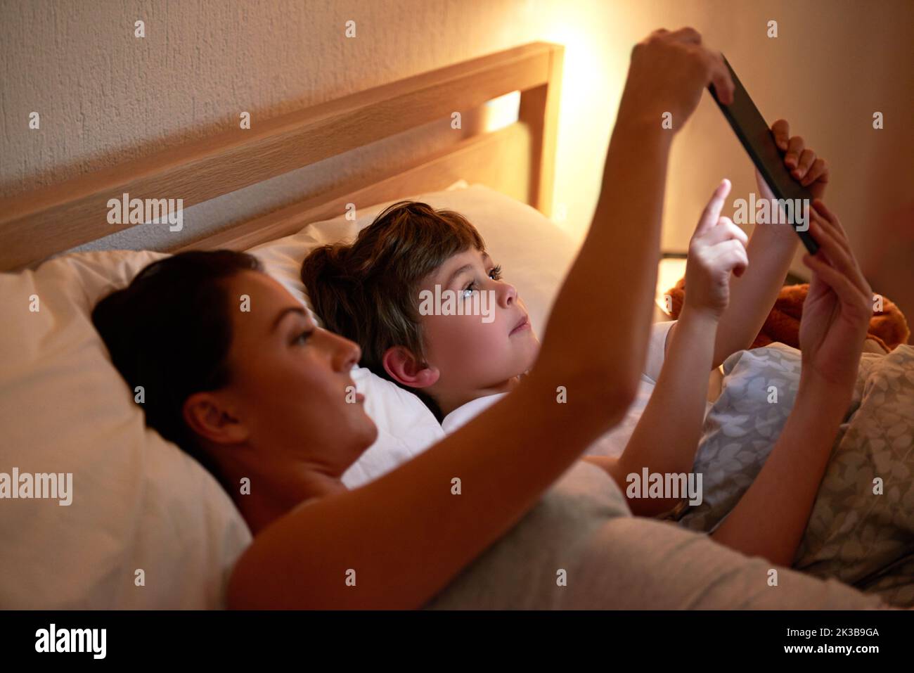 Interaktive Schlafenszeiten-Geschichten. Mutter und Sohn nutzen zusammen ein digitales Tablet, während sie im Bett liegen. Stockfoto