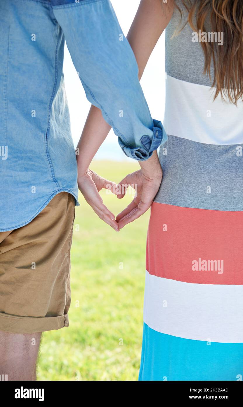 Junge Liebe. Zwei junge Menschen, die ihre Hände zusammenlegen, um eine Herzform zu bilden. Stockfoto