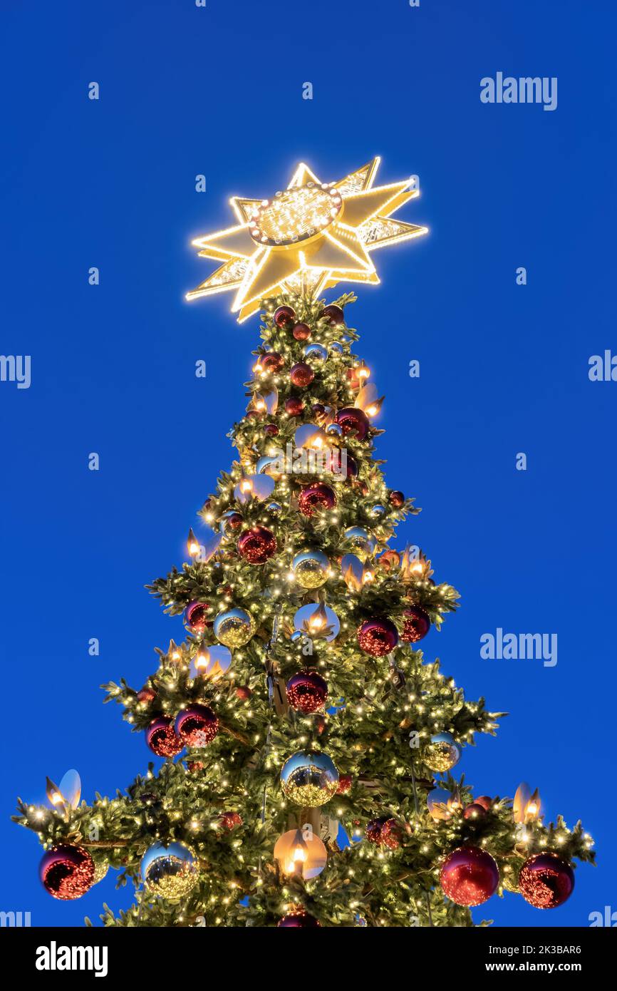 Christbaumspitze mit Bethlehem-Stern, der nachts beleuchtet wird, verziert mit Lichtern und Glaskugeln Stockfotografie