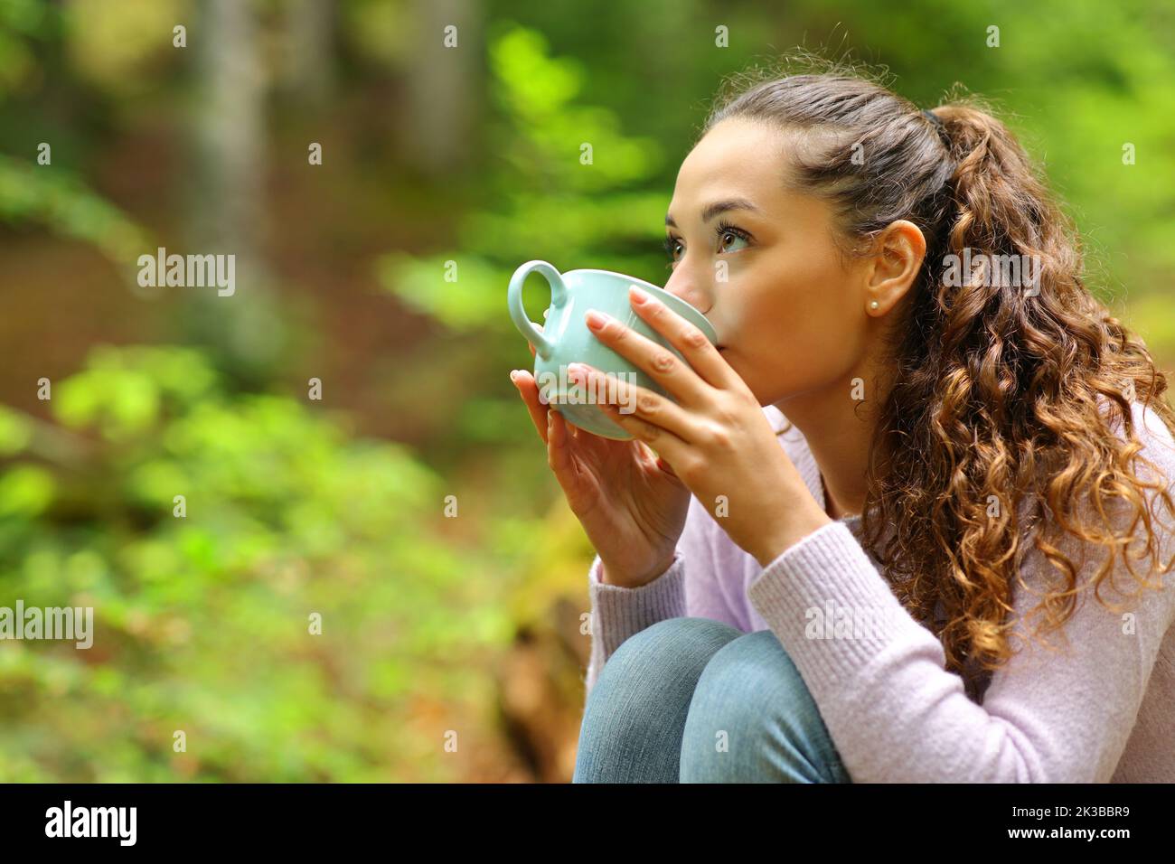 Frau, die Kaffee trinkt und oben in einem Wald schaut Stockfoto
