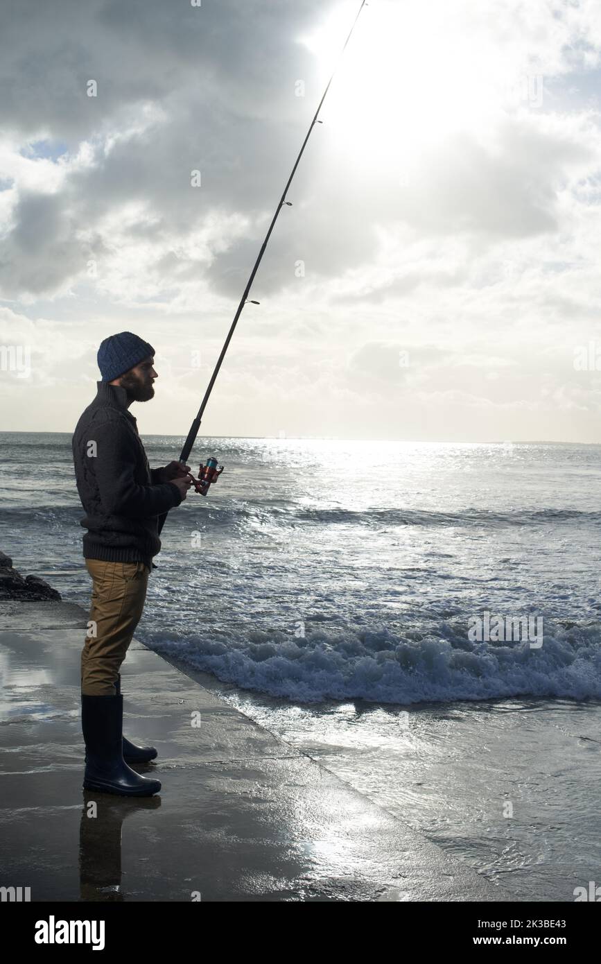 Sich Zeit für den großen Fang zu nehmen. Ganzkörperaufnahme eines Einzelfischers, der an einem Pier am Meer angeln kann. Stockfoto