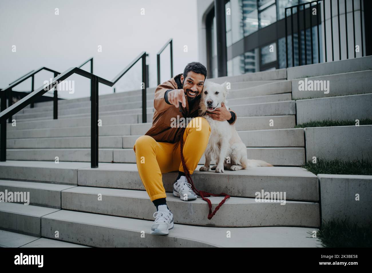 Porträt eines glücklichen jungen Mannes und seines Hundes im Freien im Treppenhaus der Stadt, Blick auf die Kamera. Stockfoto