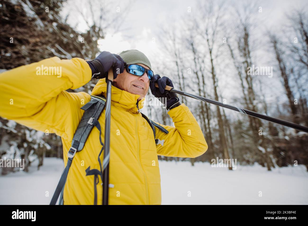 Älterer Mann, der eine Schneebrille aufsetzt und sich auf die Fahrt im verschneiten Wald vorbereitet. Stockfoto