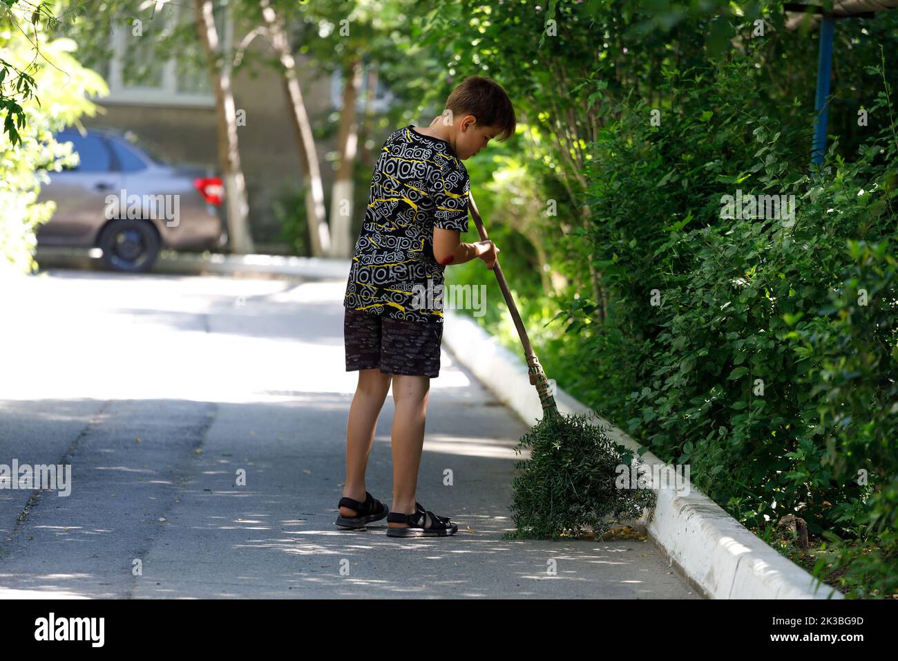 Russland Tuapse 08.08.2021 ein Junge fegt mit einem Besen im Hof eines Hauses die Straße. Hochwertige Fotos Stockfoto