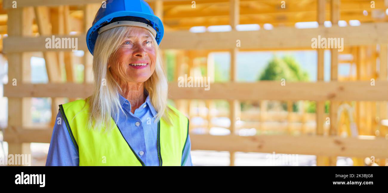 Porträt einer älteren Frau mit Schutzhelm und gelber Weste, die an einem nachhaltigen Öko-Gebäude aus Holz arbeitet. Stockfoto