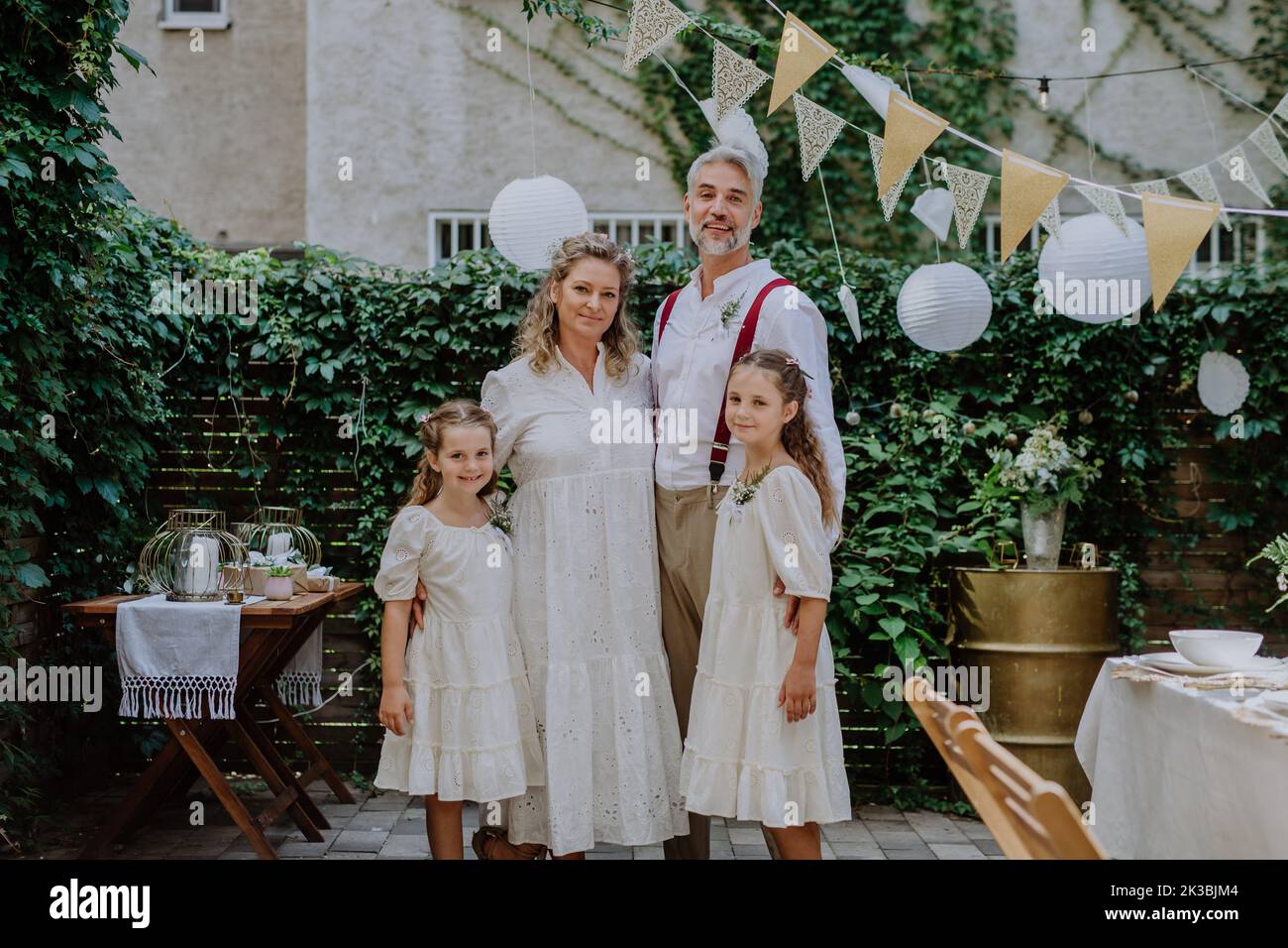 Reife Braut und Bräutigam posieren mit ihren Töchtern bei der Hochzeitsfeier draußen im Hinterhof. Stockfoto