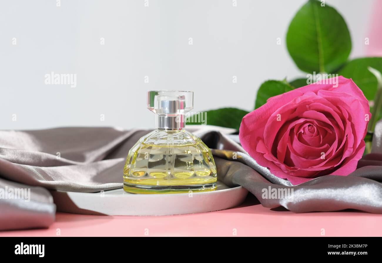 Parfümflasche, blumiger leichter Duft für Frau. Rosa Rose, Aromaspray neben Seidenbettlaken. Stockfoto