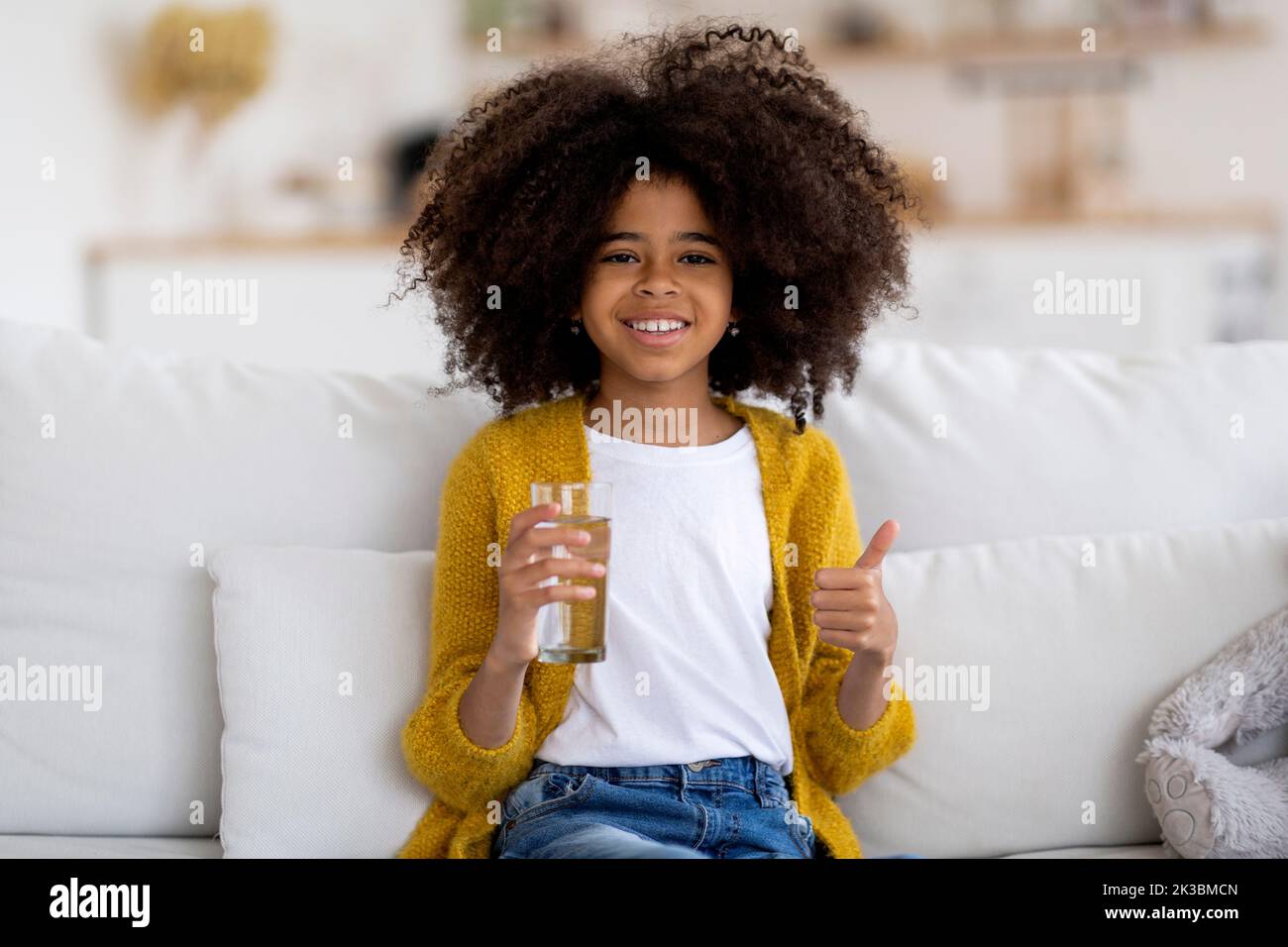 Glückliches kleines schwarzes Mädchen, das Wasser trinkt und den Daumen nach oben zeigt Stockfoto