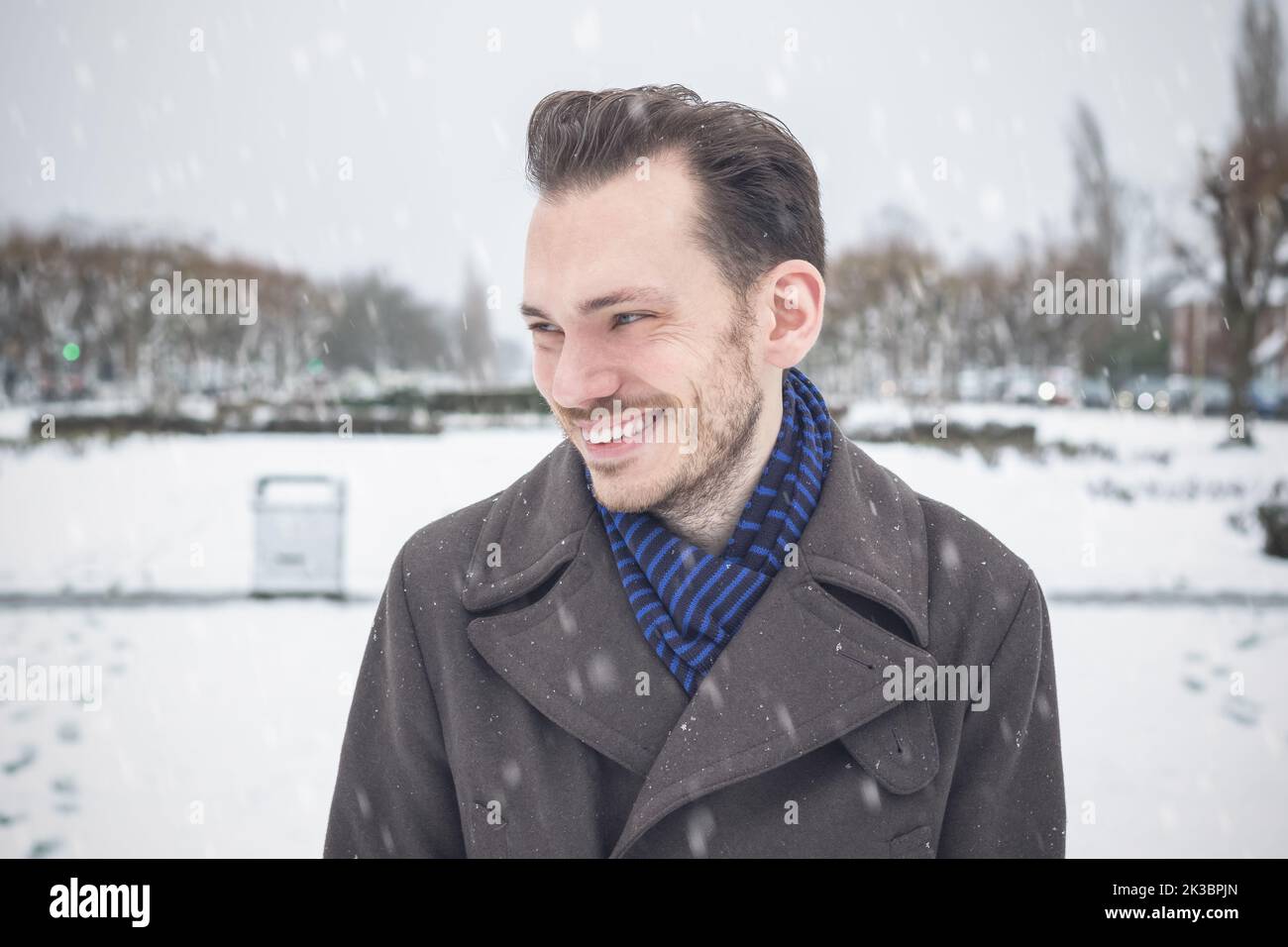 Porträt eines jungen, hübschen Mannes mit lächelndem Bart, der im Winterschnee lacht Stockfoto