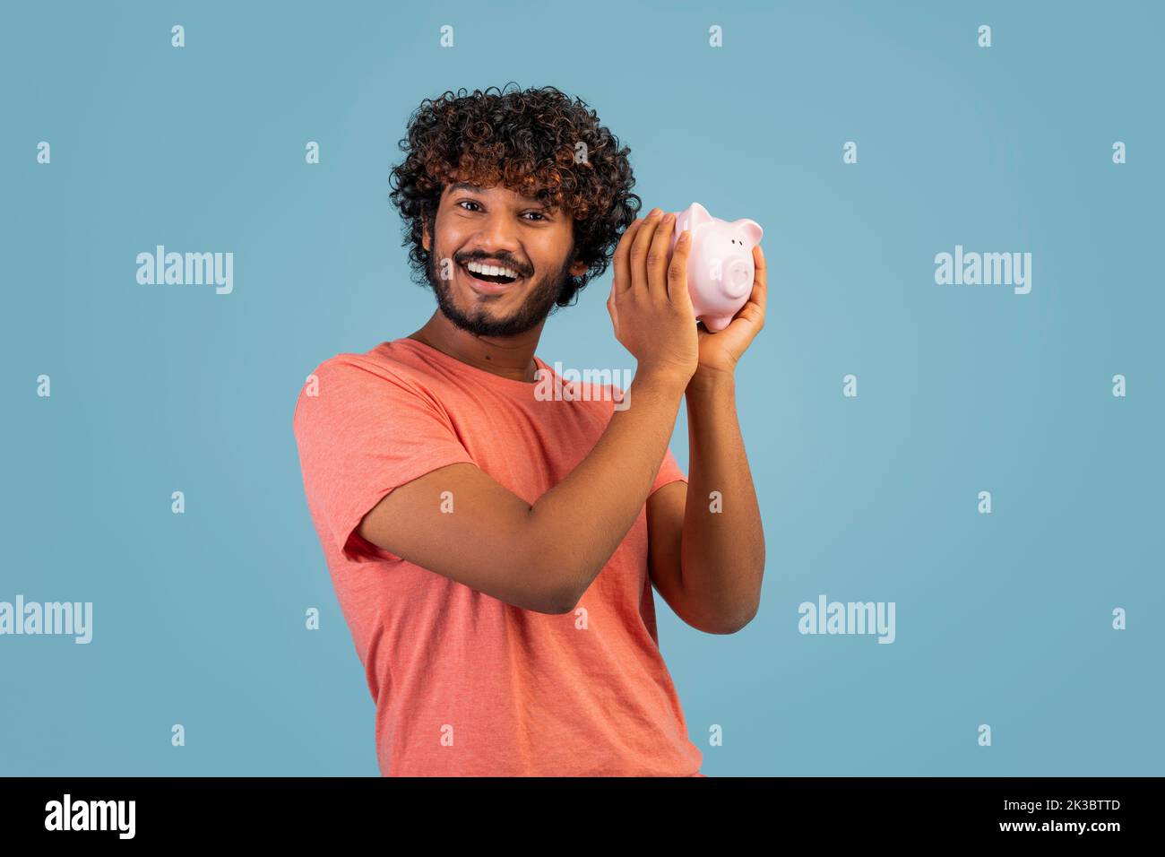 Glücklicher indischer Mann, der ein Sparschwein neben dem Ohr hält Stockfoto