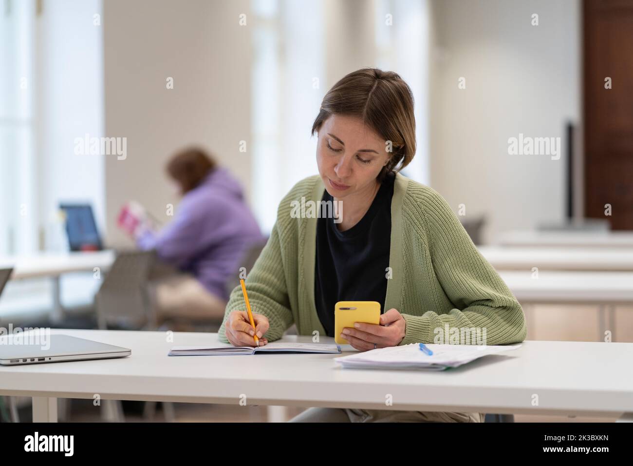 Konzentrierte reife Studentin, die Smartphone für die Prüfungsvorbereitung verwendet und den zweiten Abschluss macht Stockfoto