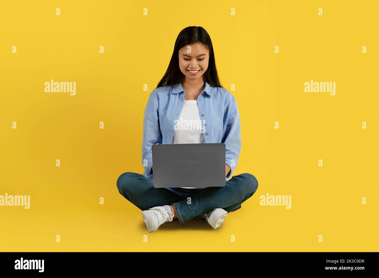 Glückliche junge koreanische Studentin in beiläufiger Schreibarbeit auf Laptop, Online-Unterricht ansehen, chatten Stockfoto
