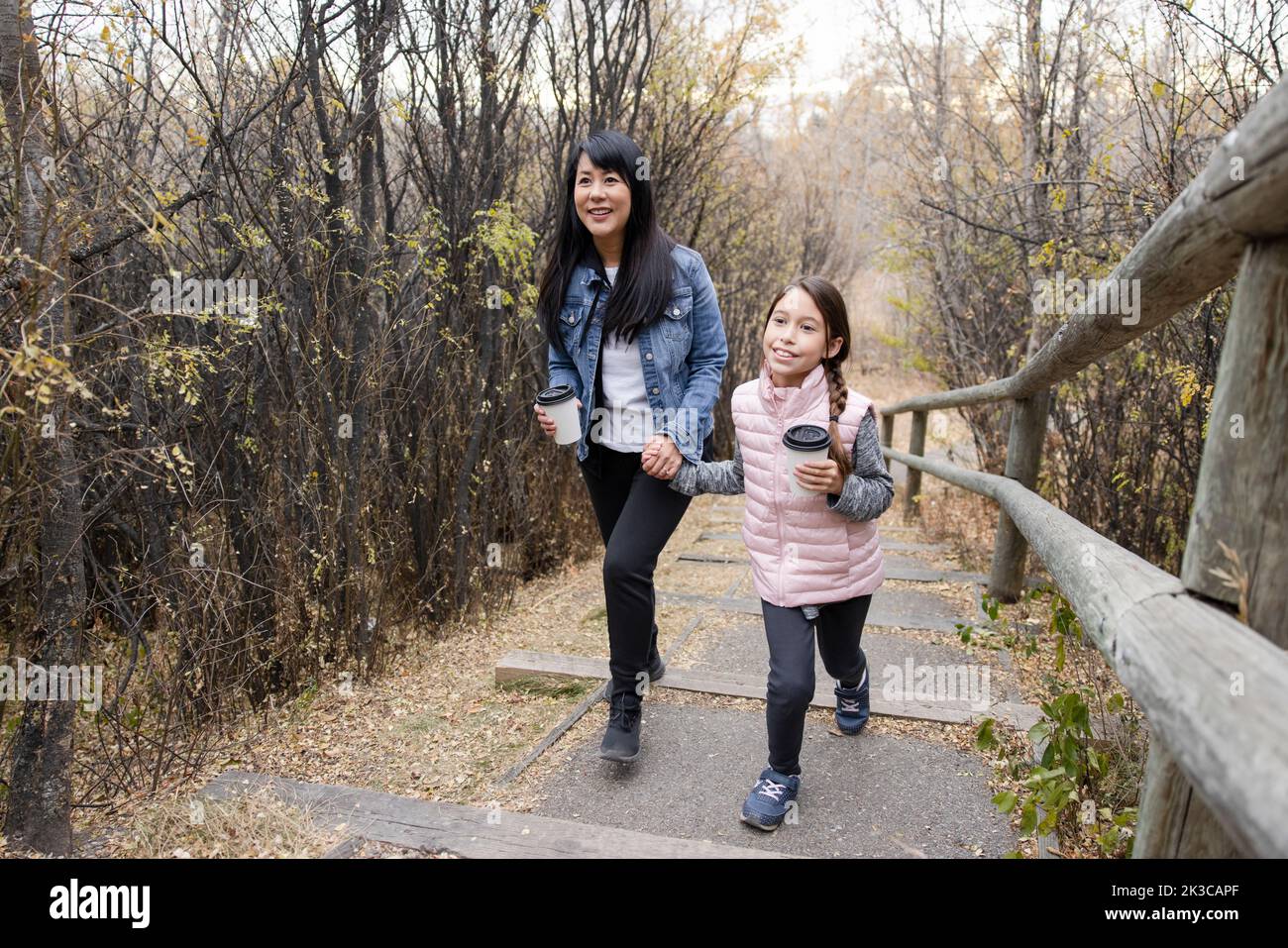 Glückliche Mutter und Tochter, die mit heißem Kakao im Herbstpark spazieren gehen Stockfoto