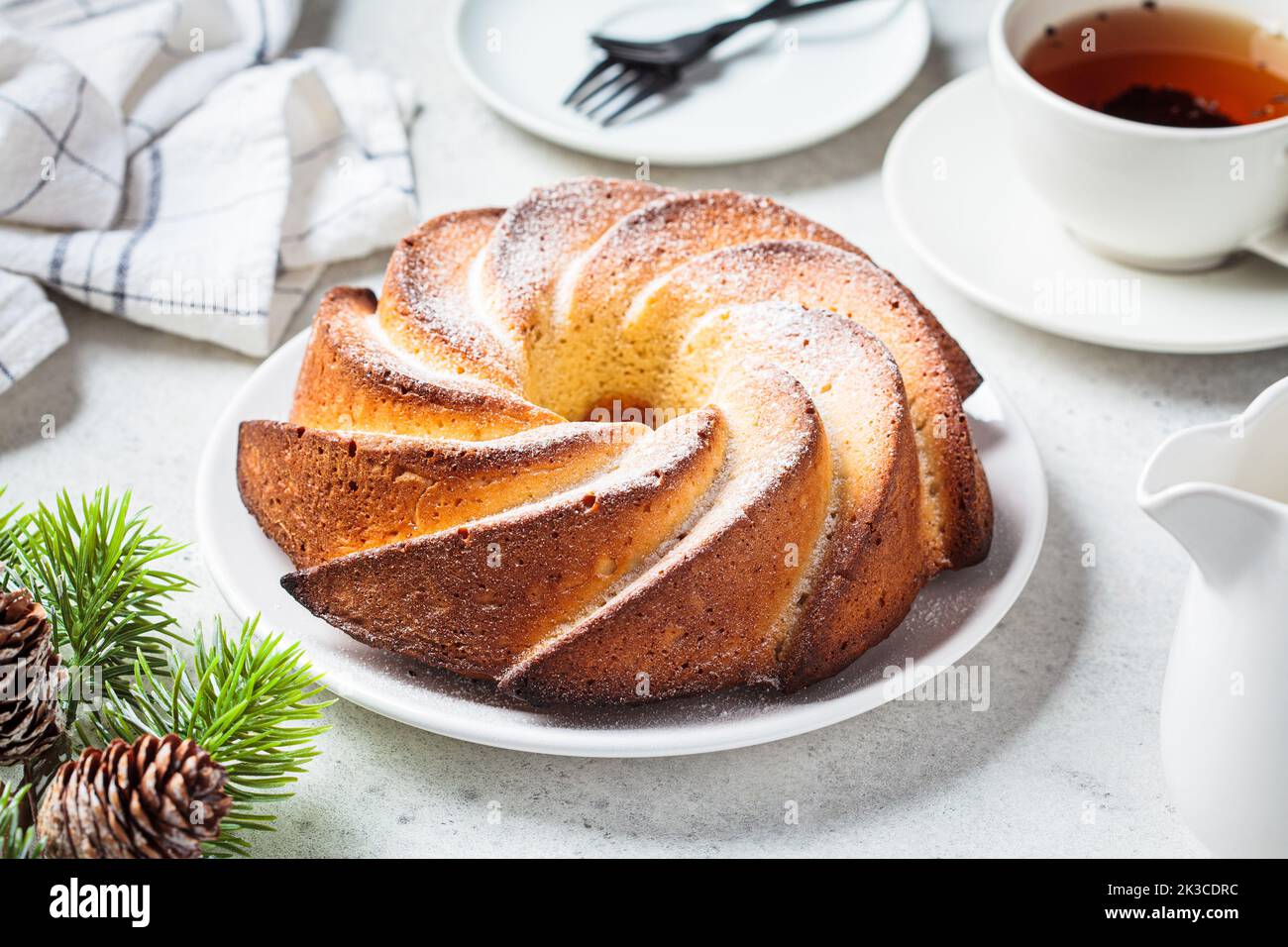 Weihnachtsdessert. Vanillekuchen mit Puderzucker auf einem weißen Teller, hellgrauer Hintergrund mit Christbaumzweigen. Stockfoto