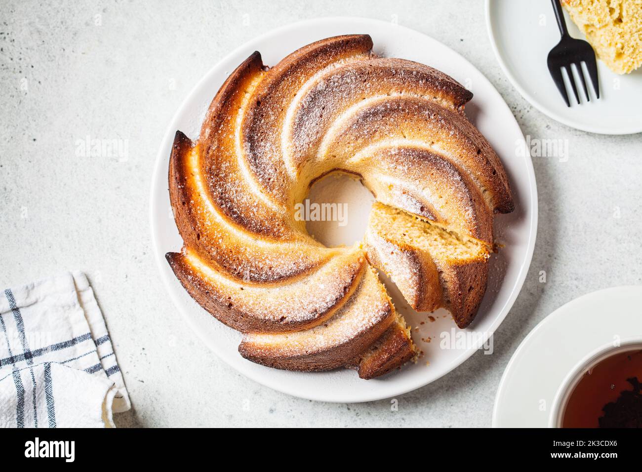Flacher Lay Vanillekuchen mit Puderzucker auf einem weißen Teller auf hellgrauem Hintergrund. Stockfoto
