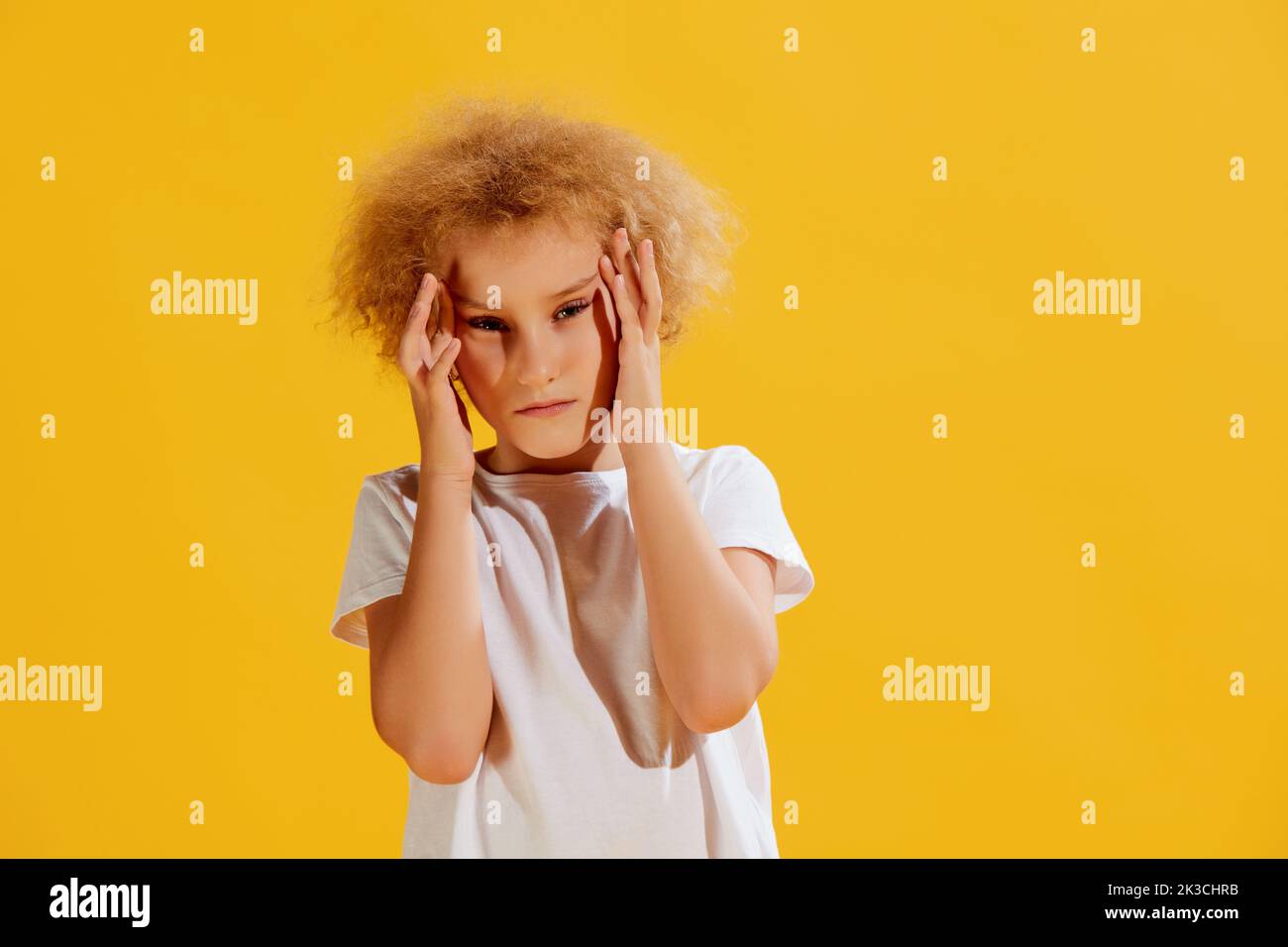 Schmerzen. Trauriges kleines Mädchen, das ihren Kopf mit Händen auf gelbem Hintergrund hält. Konzept der Kinder Emotionen, Gesundheit, Pflege, Medizin Stockfoto