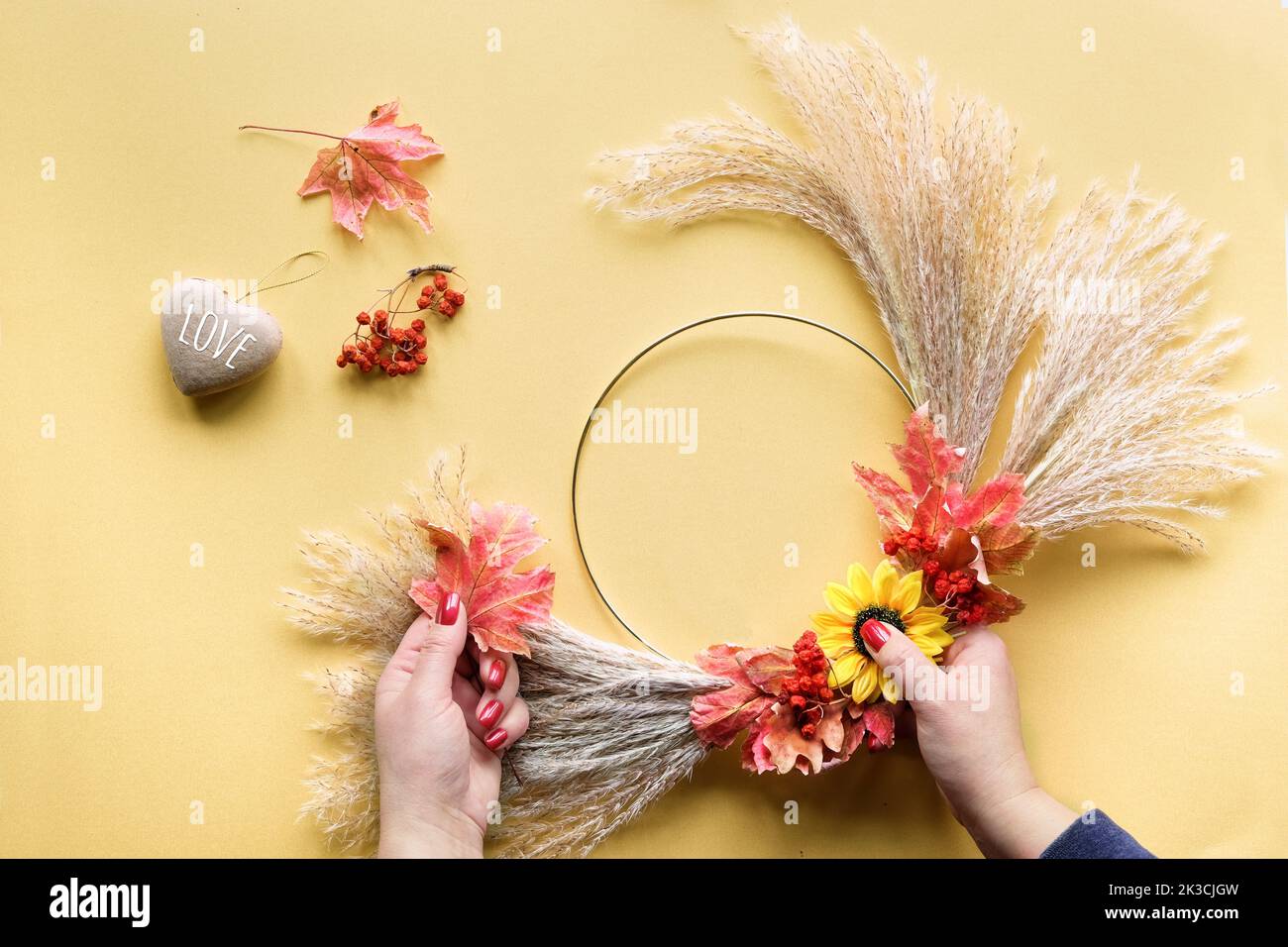 Hände, die getrockneten Blumenkranz aus trockenem Pampagras und Herbstblättern machen. Flach auf weiß gelbem Tisch, Sonnenlicht mit langen Schatten. Stockfoto