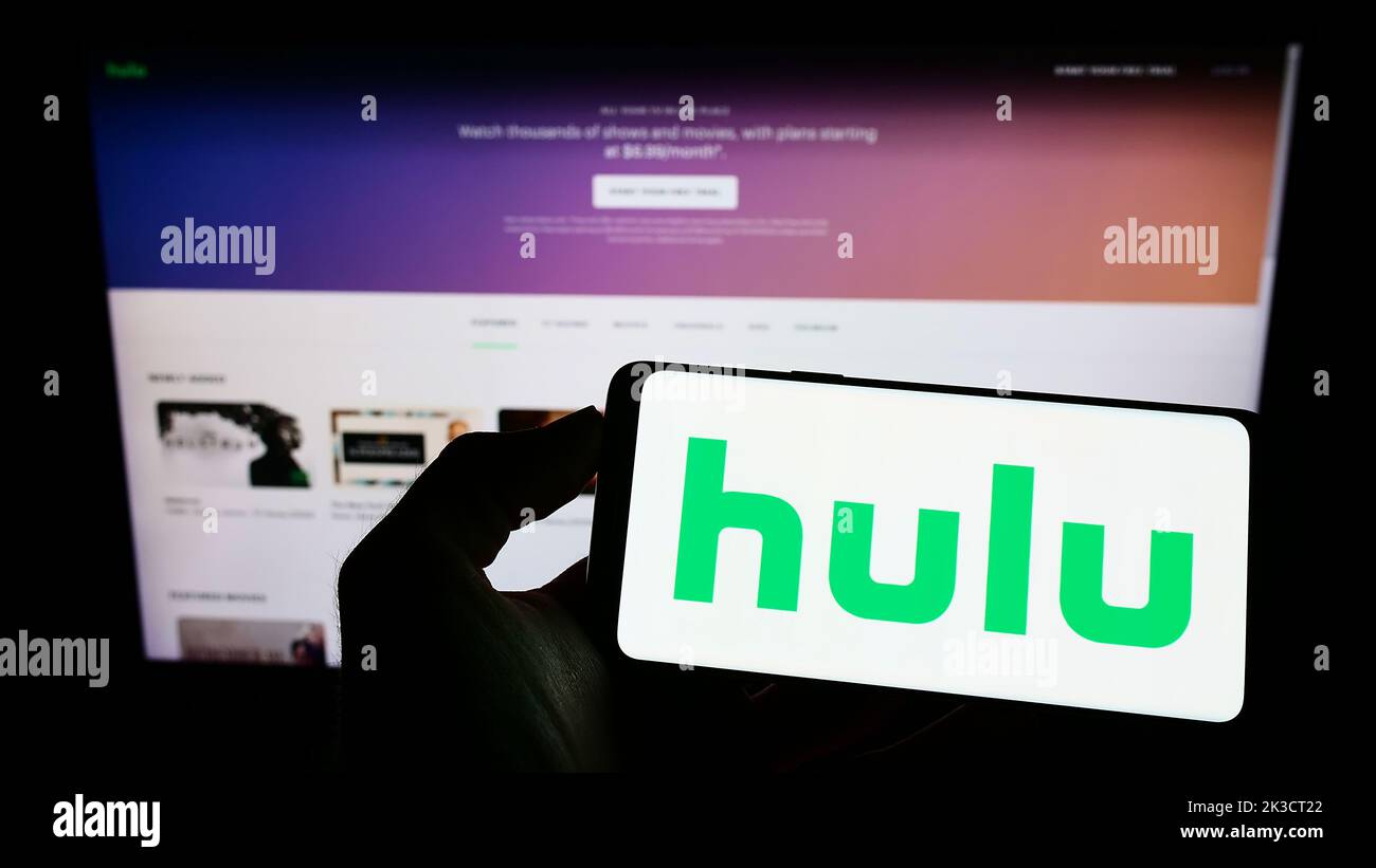 Person, die ein Mobiltelefon mit dem Logo des amerikanischen Video-Streaming-Service-Unternehmens Hulu LLC auf dem Bildschirm vor der Webseite hält. Konzentrieren Sie sich auf die Telefonanzeige. Stockfoto