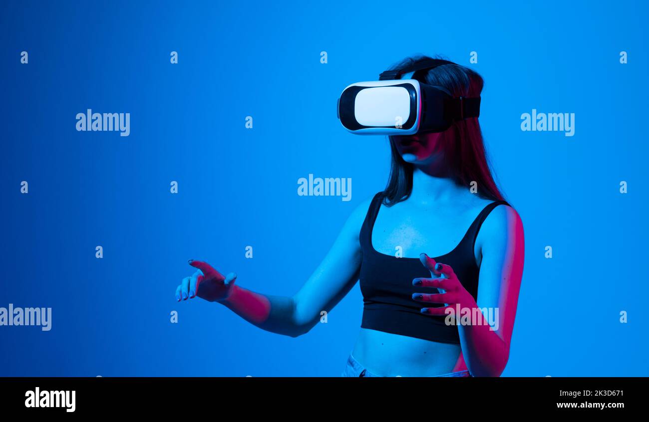 Inspirierte Brünette glückliche Frau bekommen Erfahrung mit VR-Headset-Brille der virtuellen Realität viel gestikulierende Hände in Neonlicht. Stockfoto