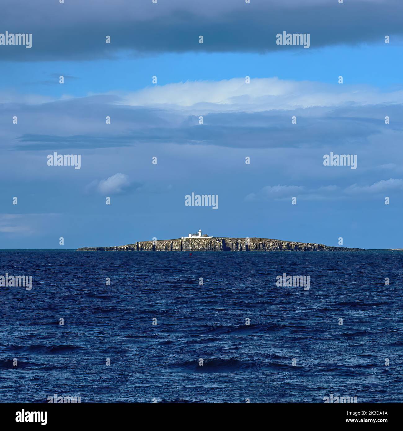 Die zerklüfteten, malerischen Farne Islands von Seahouses in scharfem Sonnenlicht, mit einer zufältigen Wolkenformation, die die Form der Insel am Horizont zu spiegeln scheint. Stockfoto