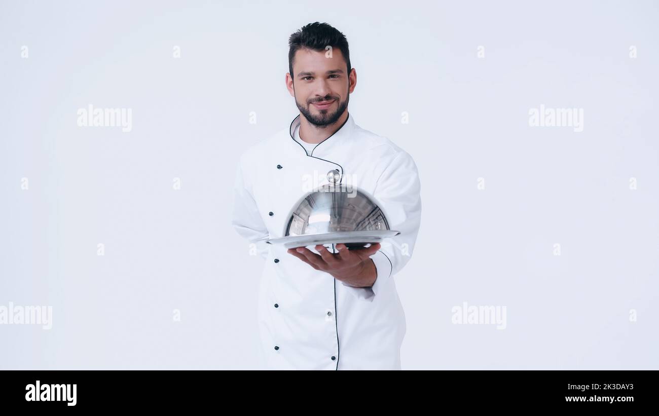 Der Koch war zufrieden mit der Servierplatte und der Cloche, die mit der Hand hinter dem Rücken auf einem weißen Bild stand Stockfoto