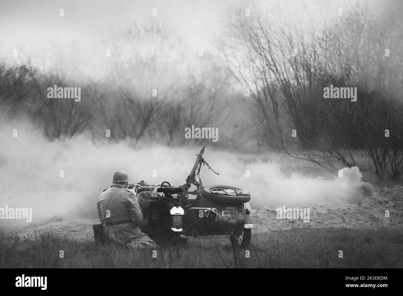Re-enactor gekleidet als Wehrmachts-Infanterie-Soldat der Zweiten Weltkrieg sitzen in der Nähe von Old Tricar, bewaffneter Maschinengewehr. Rauchwand. Armee Dreirad Motorrad Stockfoto