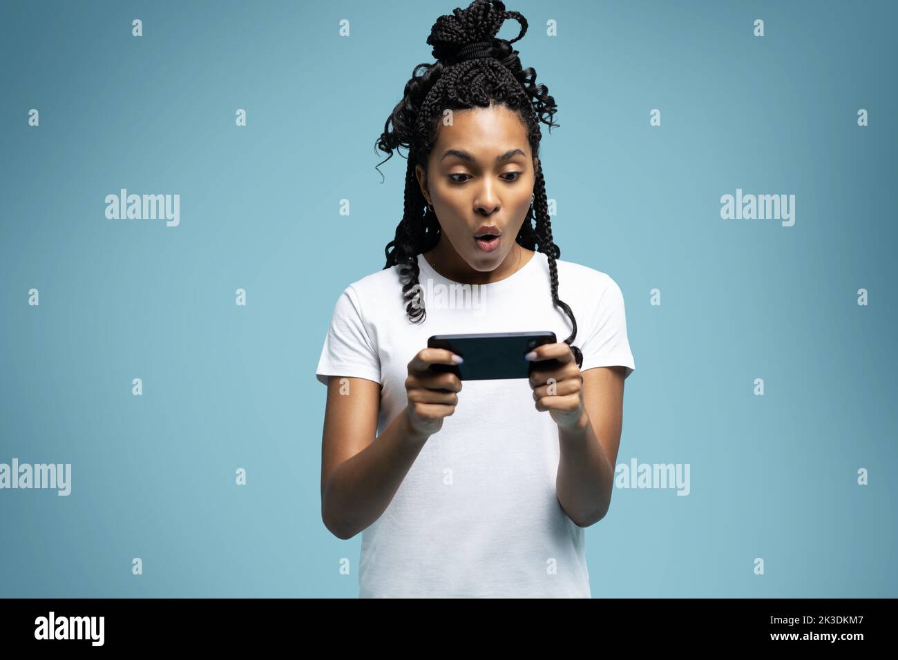 Positive lockige ethnische Frau verwendet Mobiltelefon prüft Nachrichten und liest Nachrichten hält moderne zelluläre in Händen sieht mit neugierigen glücklichen Ausdruck Stockfoto