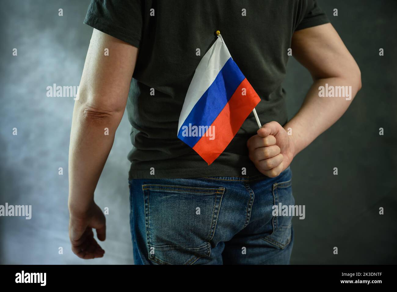 Mann versteckt russische Flagge hinter seinem Rücken, Person, die Russland liebt auf grauem Hintergrund. Konzept der Russophobie, Angst, Ukraine Krieg, Hass, Protest, Wahrheit, Stockfoto