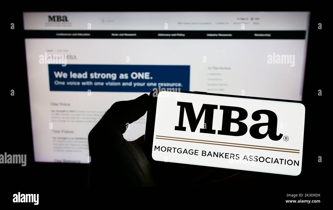 Person, die Mobiltelefon mit Logo der Organisation Mortgage Bankers Association (MBA) auf dem Bildschirm vor der Webseite hält. Konzentrieren Sie sich auf die Telefonanzeige. Stockfoto