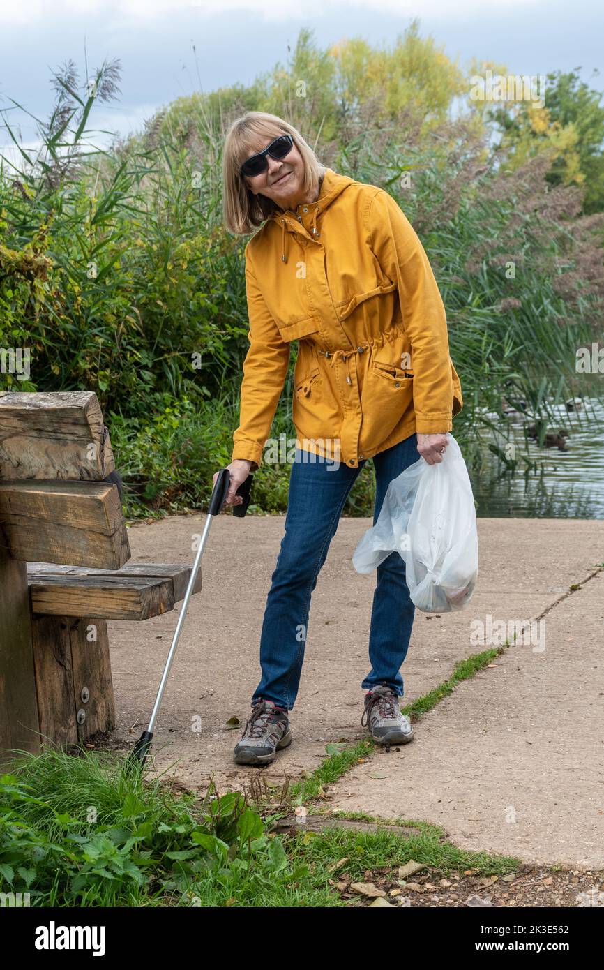Frau, die Müll pflückt, Müllsammler, die Landwege um Fleet Pond, Hampshire, England, Großbritannien aufräumen Stockfoto