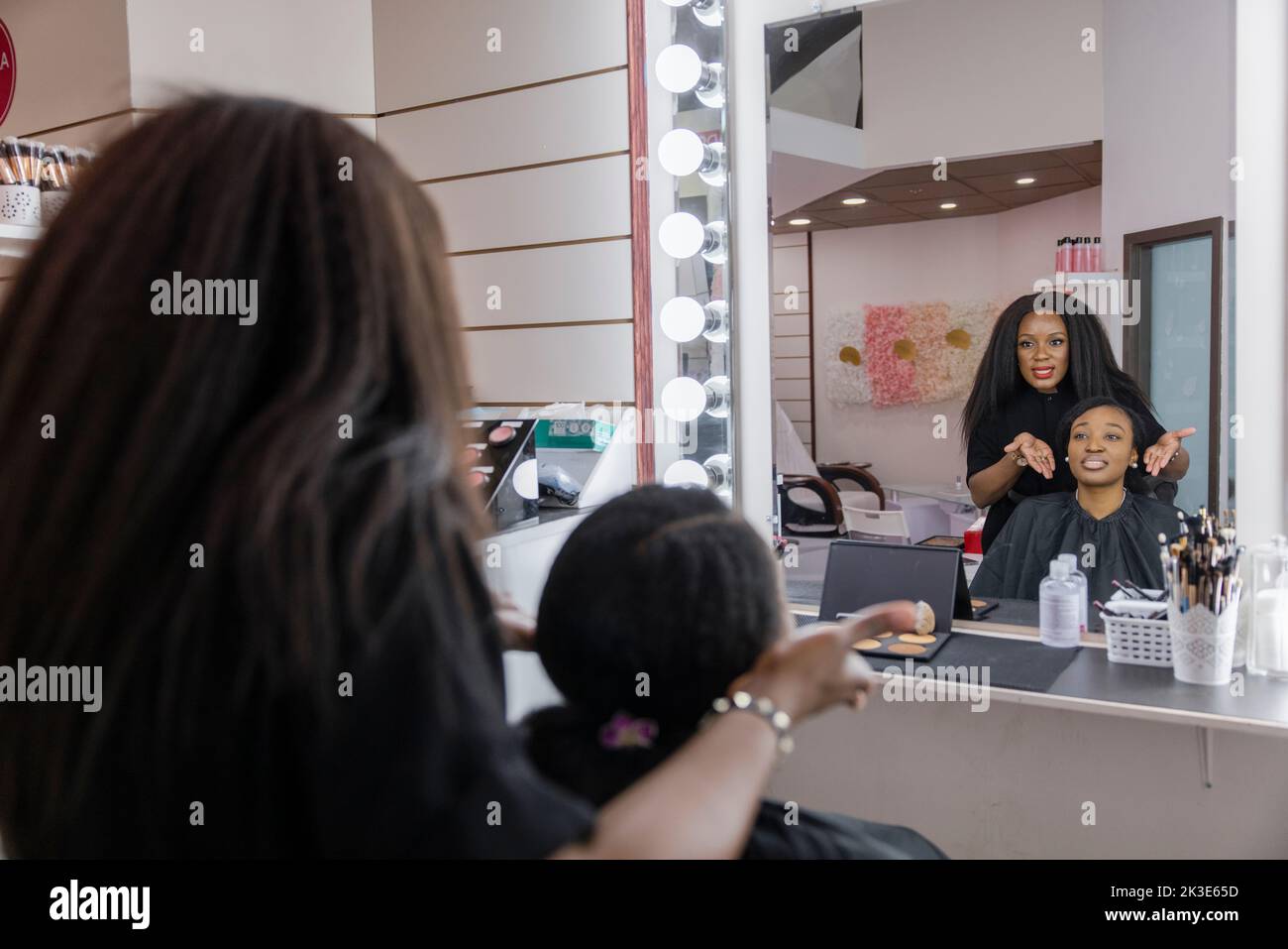 Make-up-Künstler und Kunde sprechen vor der Verjüngungskur am Spiegel Stockfoto