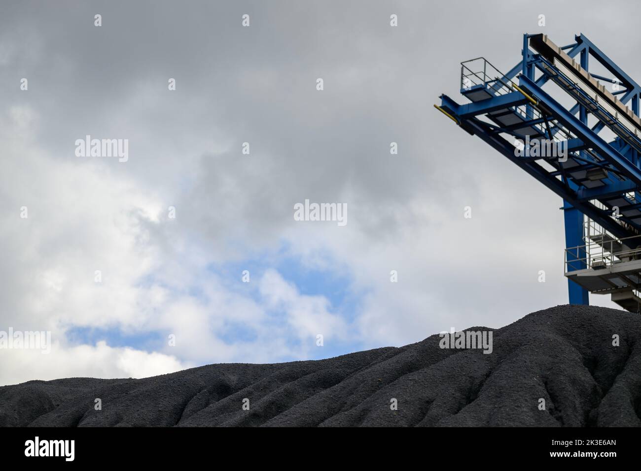 Riesiger Berg aus schwarzer Kohle und einer Stahlkonstruktion für den Transport von Kohle in einem Konzept der Energiekrise und Energieknappheit mit blauem Himmel im Hintergrund Stockfoto
