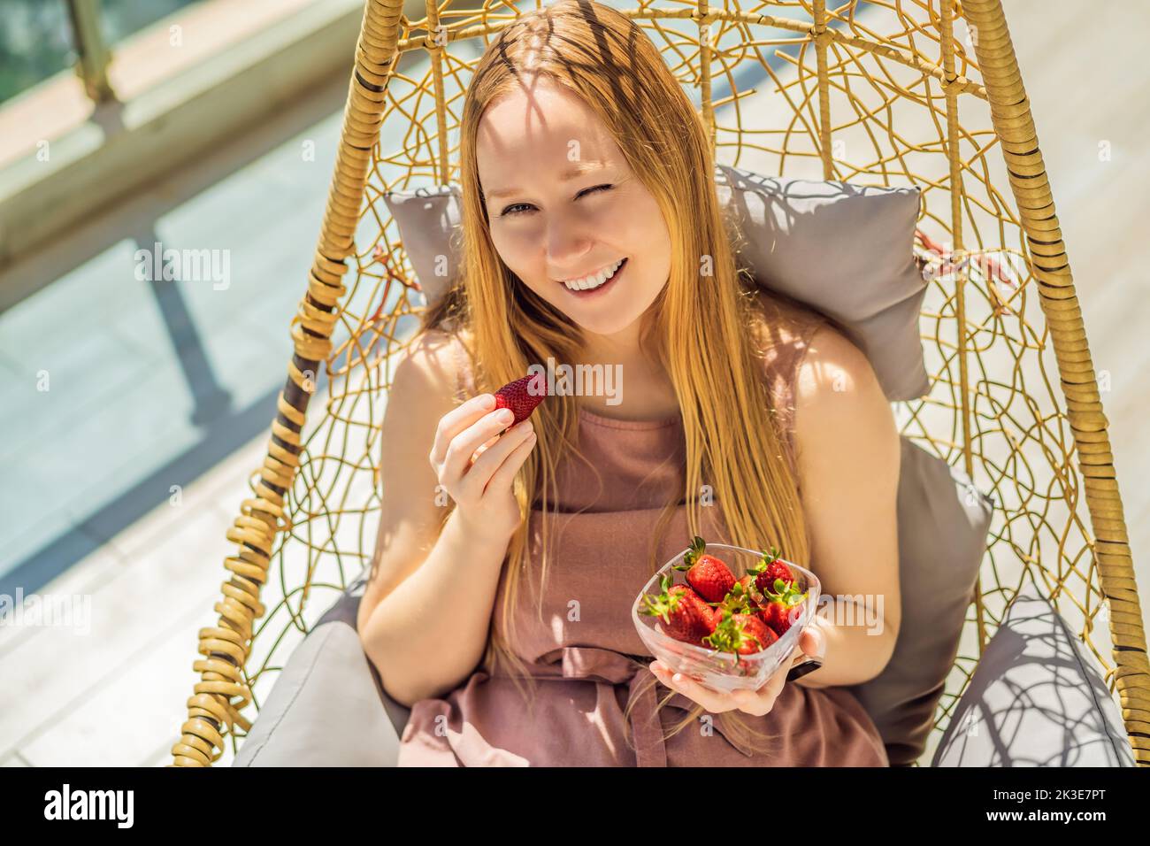 Portrait einer wunderschönen Frau in einem wunderschönen Kleid, die auf einer Terrasse sitzt und Erdbeere isst Stockfoto