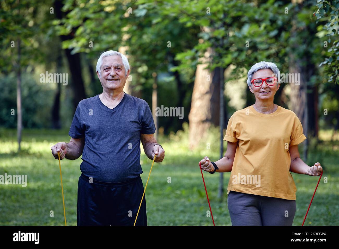 Ältere Ehegatten tragen Sportkleidung und machen morgens im Sommerpark Übungen mit Gummibändern. Gesunder Lebensstil, aktiver Ruhestand Stockfoto
