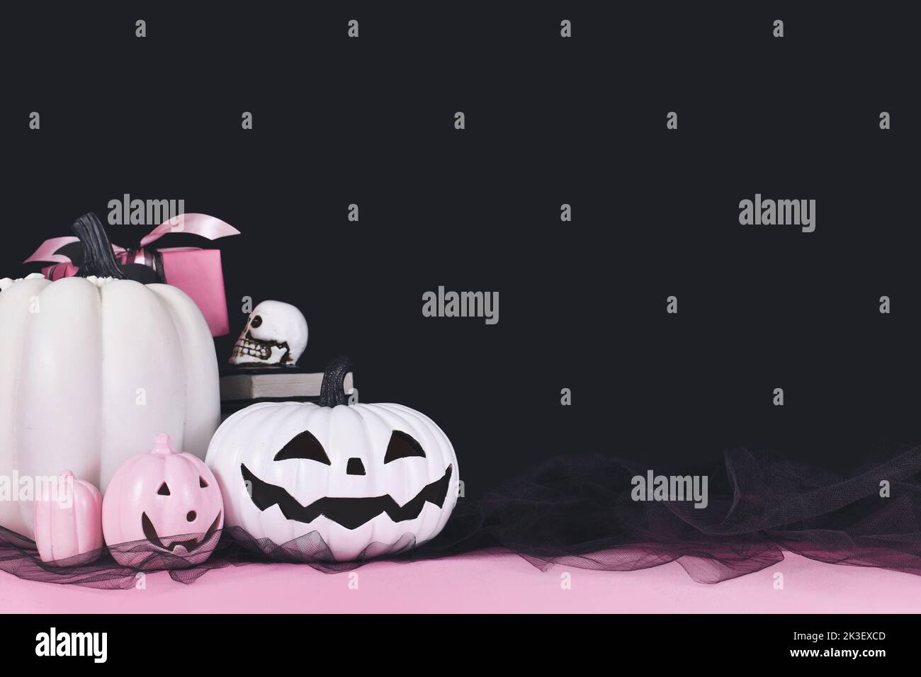 Pink-weißes Halloween Dekor mit schwarzen und weißen Kürbissen, Zauberbüchern und Spinnen auf schwarzem Hintergrund mit Kopierfläche Stockfoto