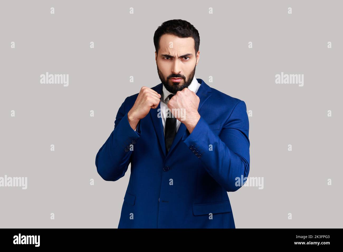 Seriöse aggressive bärtige Mann hält geballte Fäuste bereit zum Boxen, verteidigt seine Rechte und Freiheit, trägt offiziellen Stil Anzug. Innenaufnahme des Studios isoliert auf grauem Hintergrund. Stockfoto