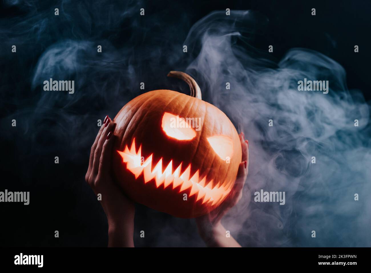 Dampfender Kürbis, der übel lacht - Kopf der Laterne mit geschnitzten Augen und bösem Grinsen auf Rauchhintergrund. Symbol für Halloween, Trick or Treat. Stockfoto