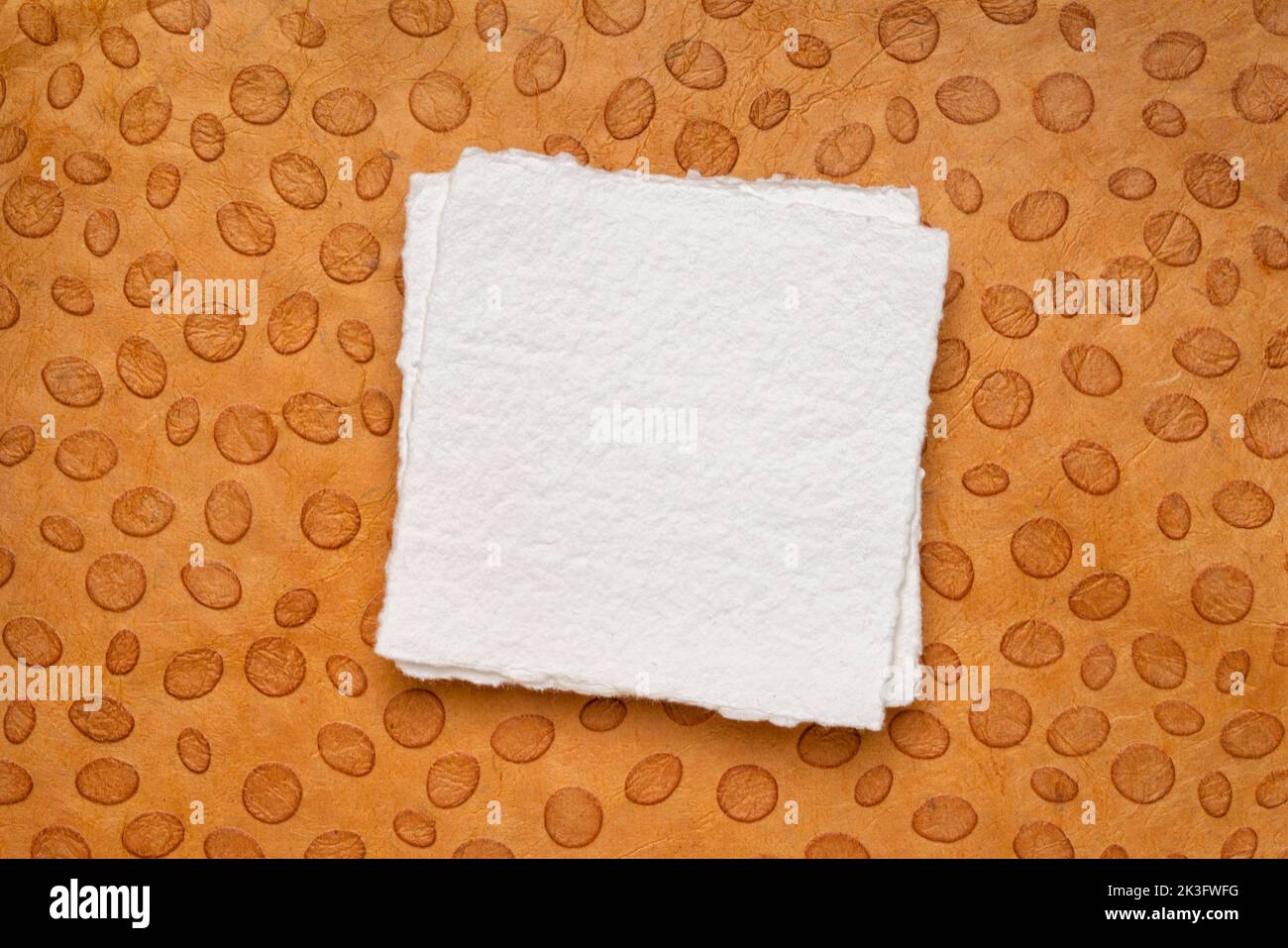 Kleines quadratisches Blatt weißes Khadi-Papier gegen orangefarbenes Papier mit Punktmuster Stockfoto