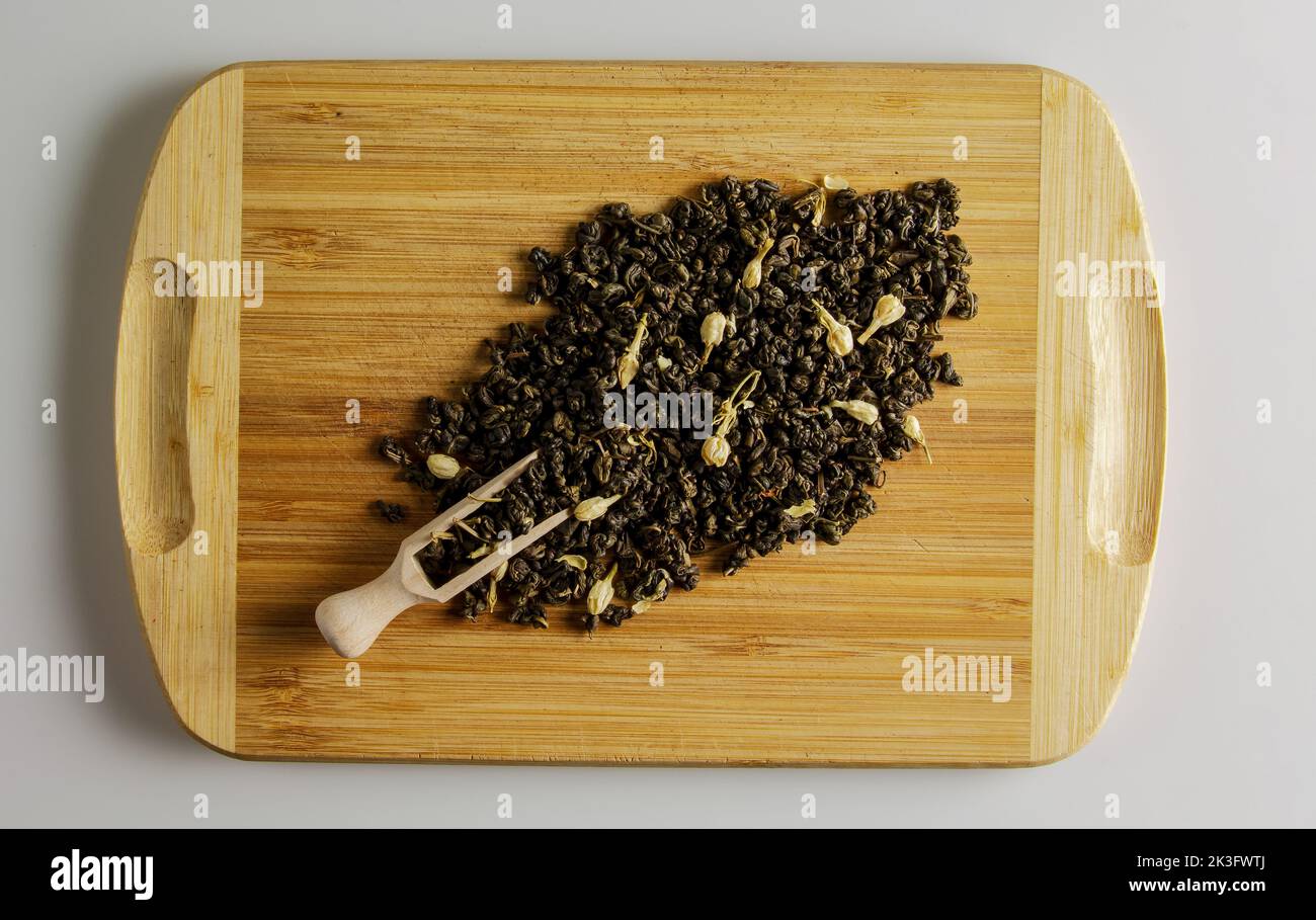 Grüner Tee mit Jasminblüten und Knospen. Holzspatel mit Tee und einer Handvoll Teemischung auf einem Holzbrett. Stockfoto